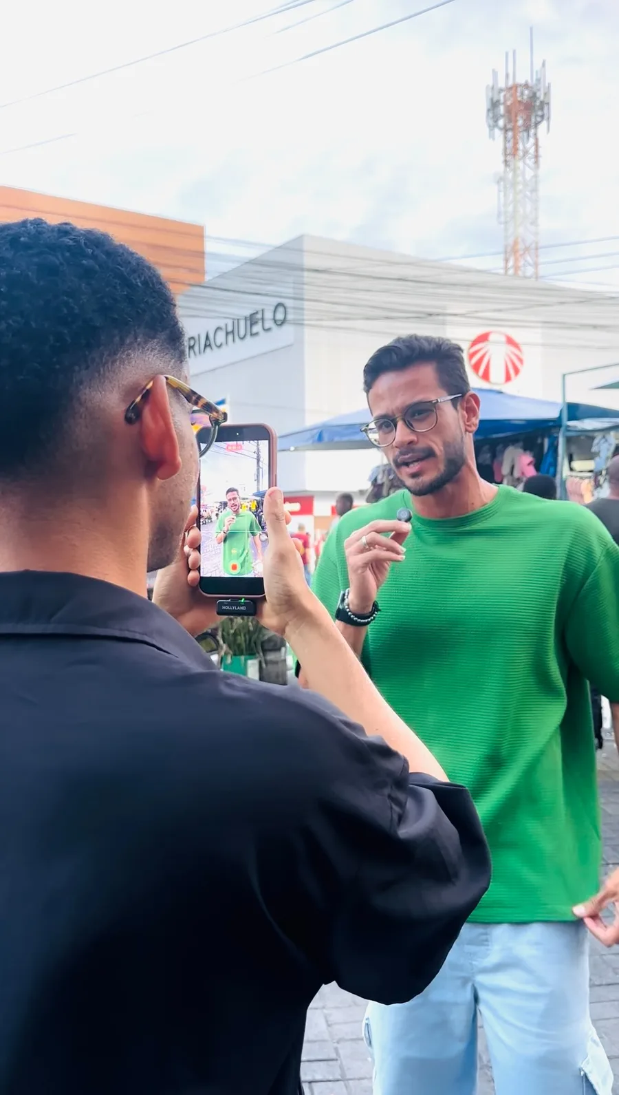 Yugui Alves sendo filmado na rua, em frente a uma loja, sem nenhuma estrutura de estúdio